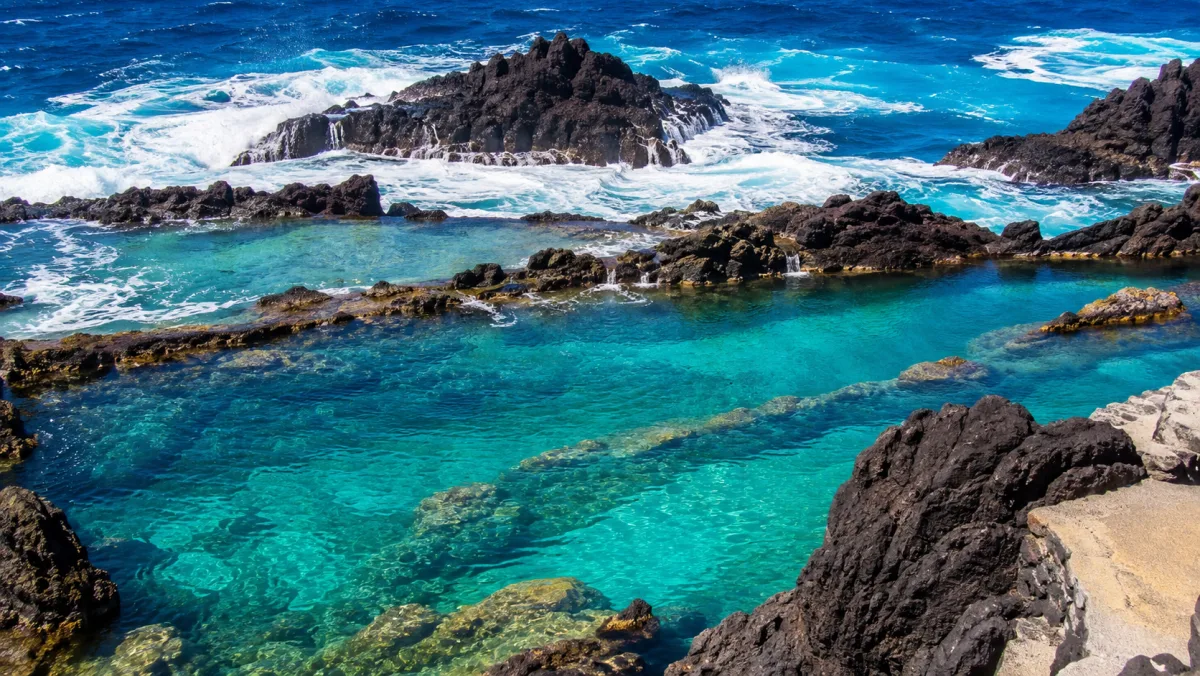 Piscinas naturales volcánicas de Porto Moniz con agua turquesa entre roca negra y el Atlántico rompiendo detrás, en la costa norte de Madeira
